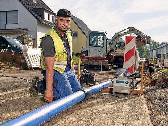 Mann hockt an Baustelle vor Rohr und schaut in die Kamera