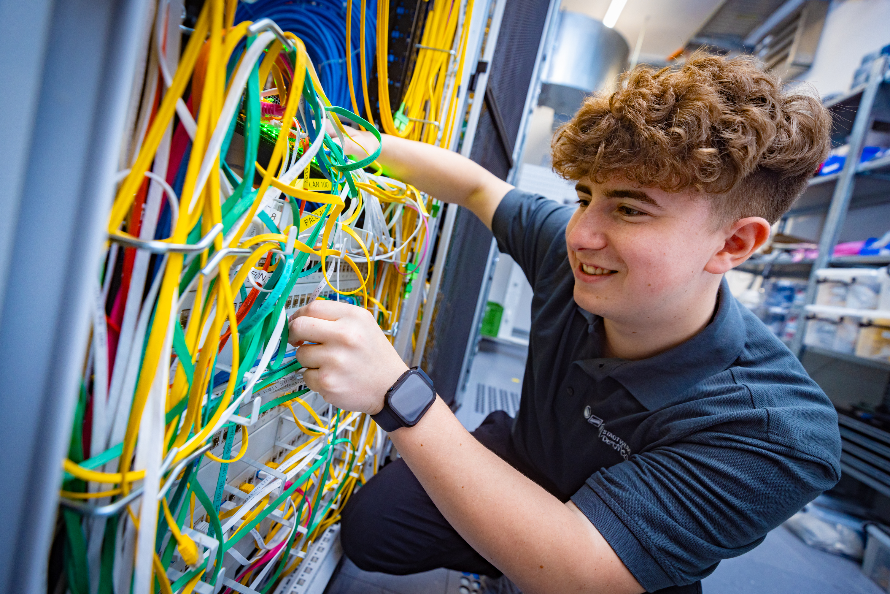 Auszubildener für Fachinformatiker für Systemintegration steckt im Serverraum bunte Kabel im Kabelschrank um